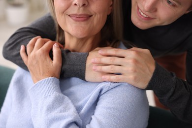 Photo of Smiling son hugging his mother indoors, closeup