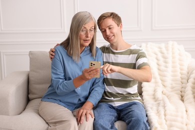 Photo of Happy son and his mother using smartphone on sofa at home