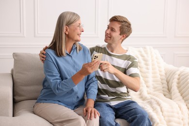 Photo of Happy son and his mother using smartphone on sofa at home