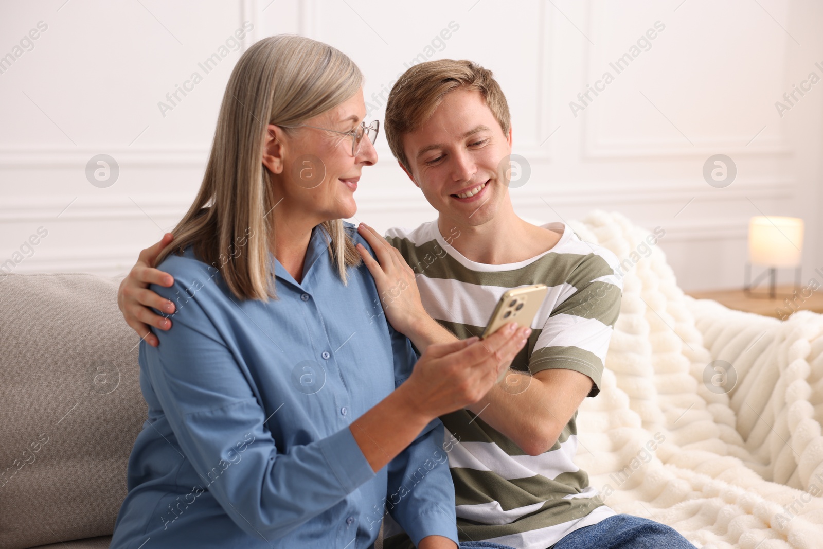 Photo of Happy son and his mother using smartphone on sofa at home