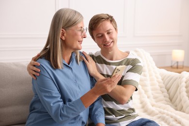 Photo of Happy son and his mother using smartphone on sofa at home