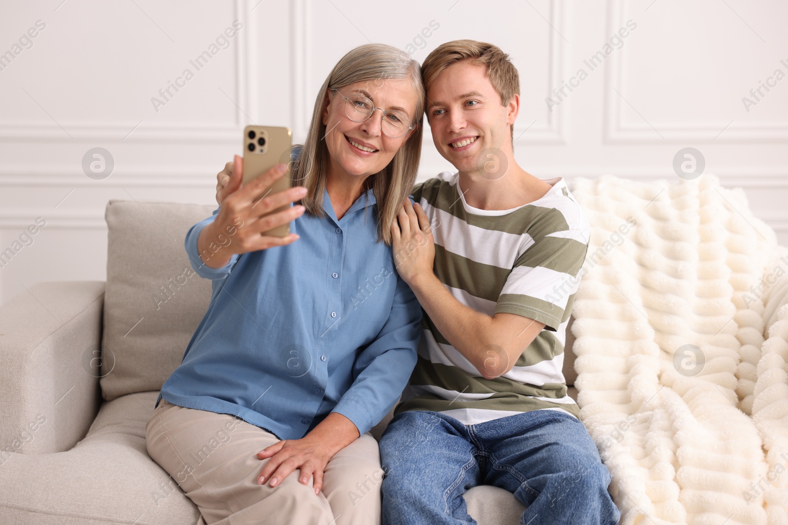Photo of Happy son and his mother taking selfie on sofa at home
