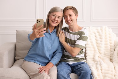 Photo of Happy son and his mother taking selfie on sofa at home
