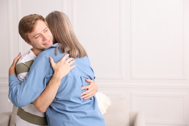 Photo of Smiling son hugging his mother at home. Space for text