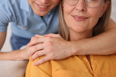 Photo of Smiling son hugging his mother indoors, closeup