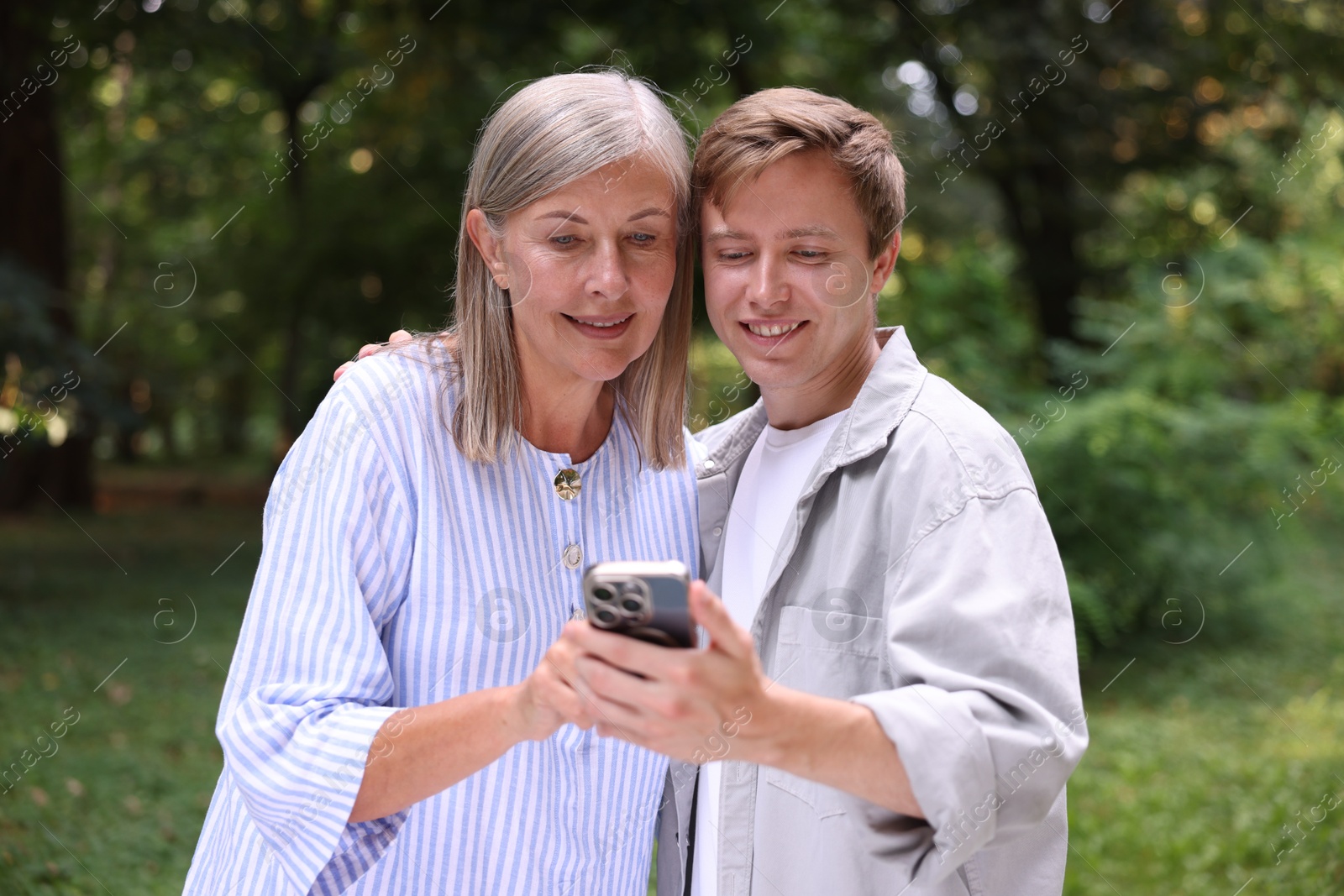 Photo of Smiling mother and her son using smartphone outdoors