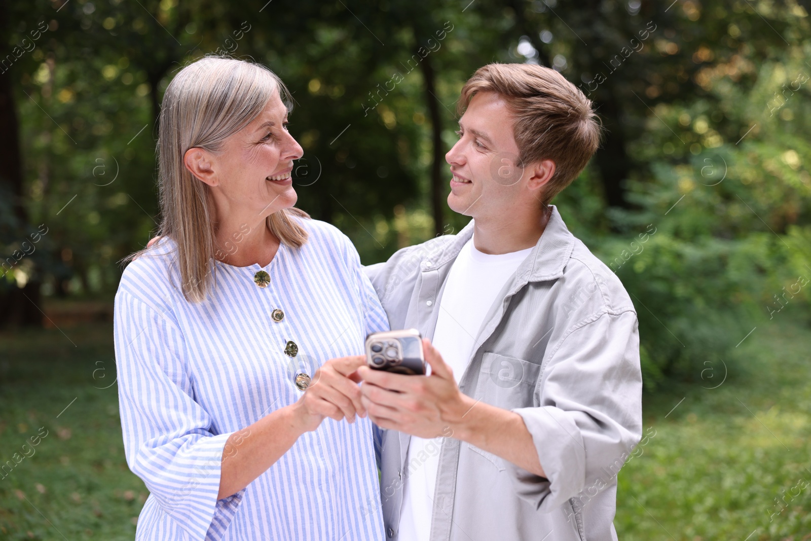 Photo of Smiling mother and her son with smartphone outdoors