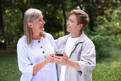 Photo of Smiling mother and her son with smartphone outdoors