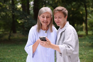 Photo of Smiling mother and her son using smartphone outdoors. Space for text