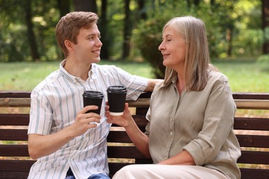 Photo of Mother and her son drinking coffee together on bench in park