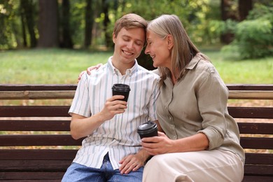 Photo of Smiling mother and her son drinking coffee together on bench in park