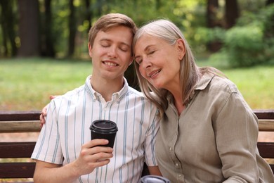 Photo of Smiling mother and her son drinking coffee together on bench in park