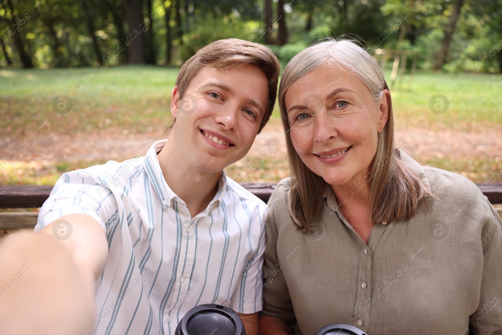 Photo of Smiling son and his mother taking selfie on bench in park