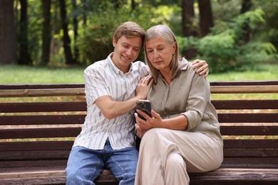 Photo of Mother and her son using smartphone on bench in park