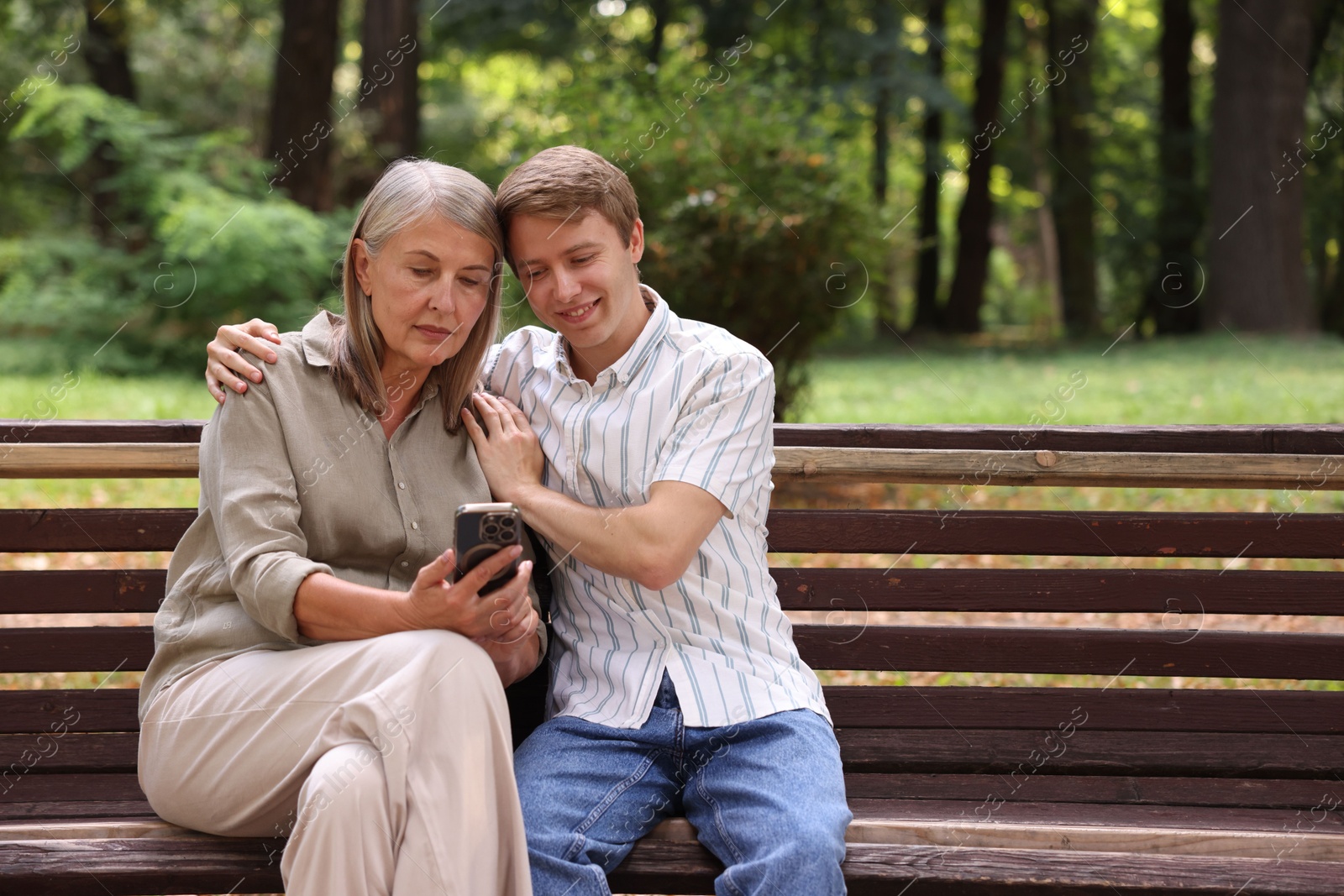 Photo of Mother and her son using smartphone on bench in park. Space for text