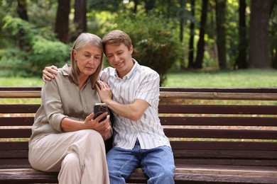 Photo of Mother and her son using smartphone on bench in park. Space for text