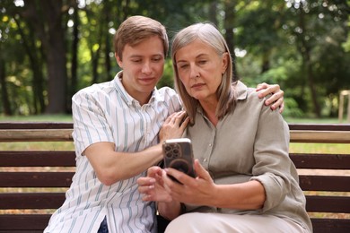 Photo of Mother and her son using smartphone on bench in park