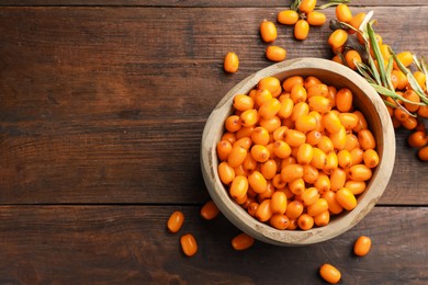 Photo of Fresh sea buckthorn berries in bowl and leaves on wooden table, flat lay. Space for text