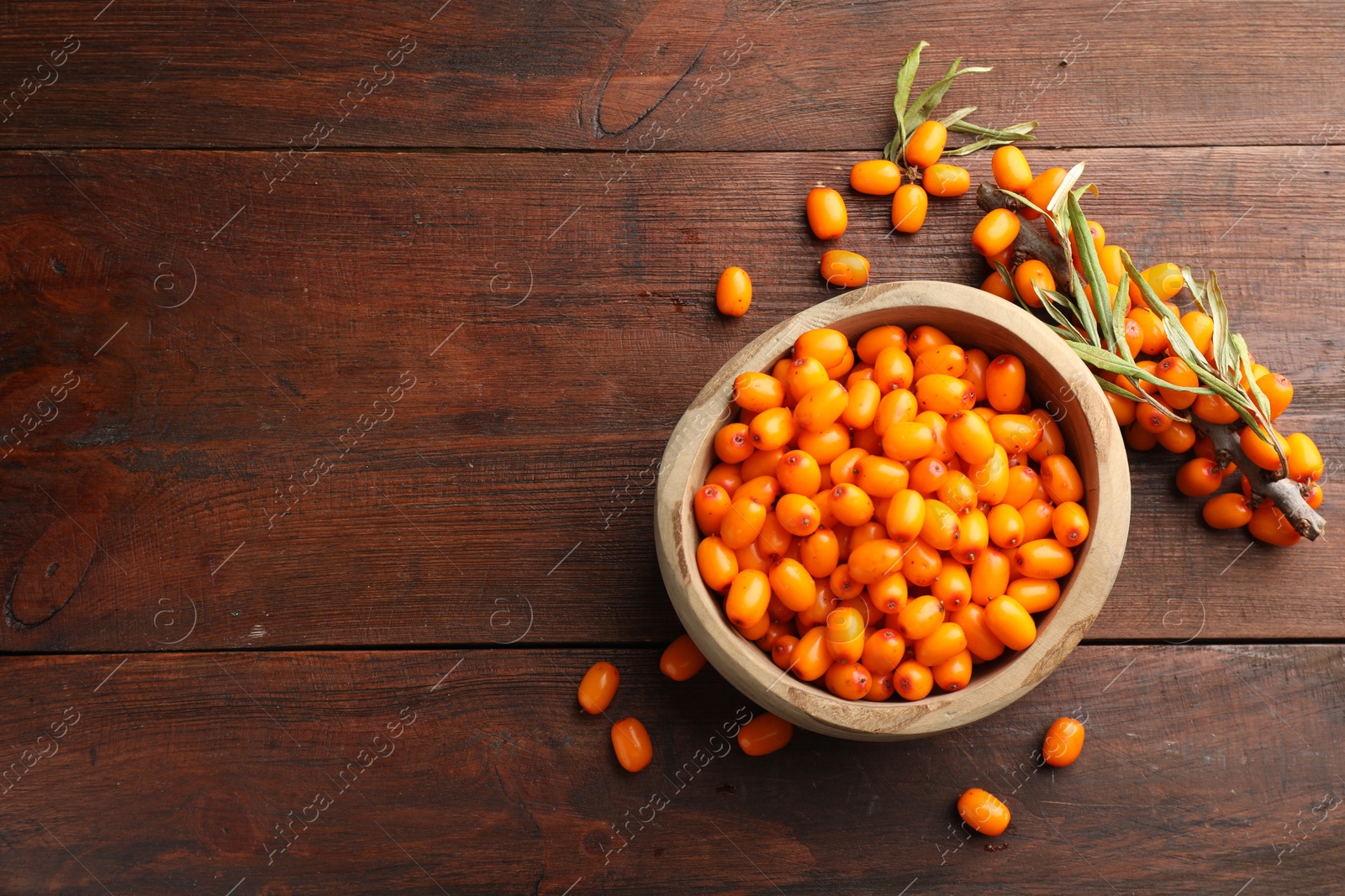 Photo of Fresh sea buckthorn berries in bowl and leaves on wooden table, flat lay. Space for text