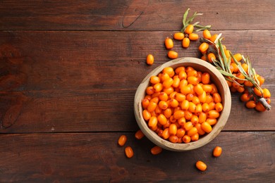 Photo of Fresh sea buckthorn berries in bowl and leaves on wooden table, flat lay. Space for text