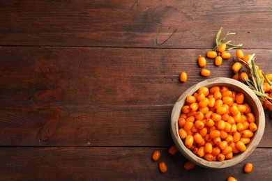 Photo of Fresh sea buckthorn berries in bowl and leaves on wooden table, flat lay. Space for text