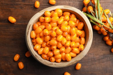 Photo of Fresh sea buckthorn berries in bowl and leaves on wooden table, flat lay