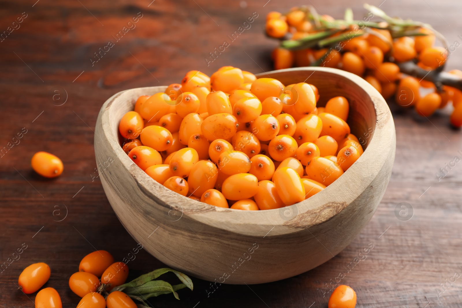 Photo of Fresh sea buckthorn berries in bowl and leaves on wooden table, closeup