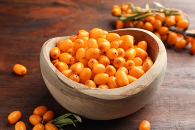 Photo of Fresh sea buckthorn berries in bowl and leaves on wooden table, closeup