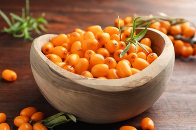 Photo of Fresh sea buckthorn berries in bowl and leaves on wooden table, closeup