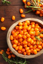 Photo of Fresh sea buckthorn berries in bowl and leaves on wooden table, flat lay