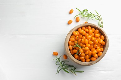 Photo of Fresh sea buckthorn berries in bowl and leaves on white wooden table, flat lay. Space for text