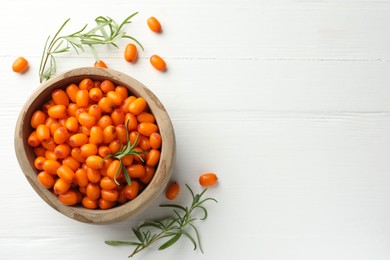 Photo of Fresh sea buckthorn berries in bowl and leaves on white wooden table, flat lay. Space for text