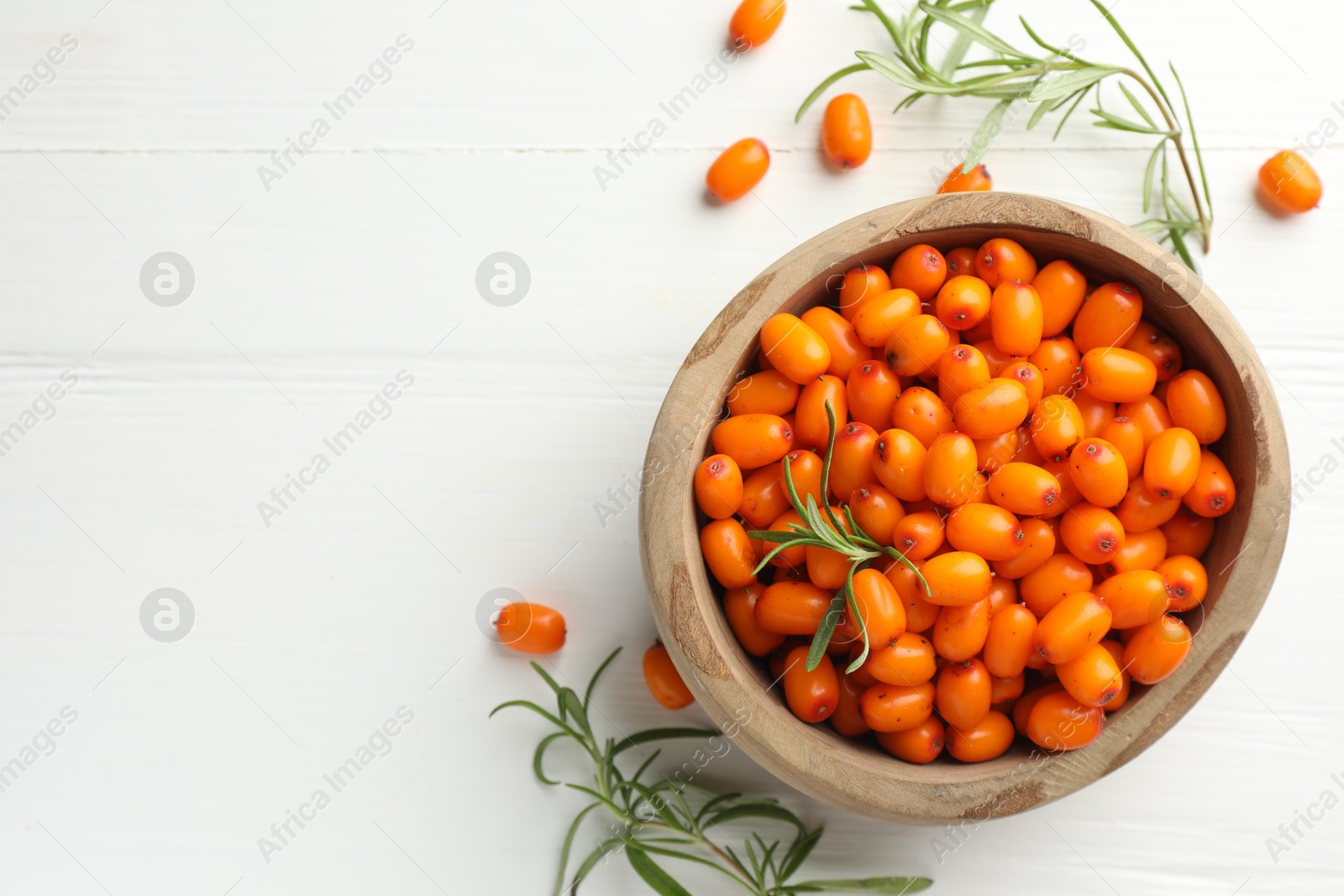 Photo of Fresh sea buckthorn berries in bowl and leaves on white wooden table, flat lay. Space for text