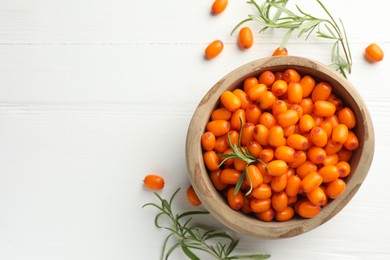 Photo of Fresh sea buckthorn berries in bowl and leaves on white wooden table, flat lay. Space for text