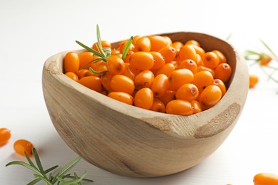 Photo of Fresh sea buckthorn berries in bowl and leaves on white wooden table, closeup