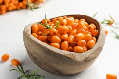 Photo of Fresh sea buckthorn berries in bowl and leaves on white wooden table, closeup