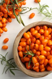 Photo of Fresh sea buckthorn berries in bowl and leaves on white wooden table, flat lay