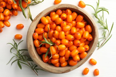 Photo of Fresh sea buckthorn berries in bowl and leaves on white wooden table, flat lay