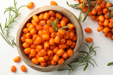 Photo of Fresh sea buckthorn berries in bowl and leaves on white wooden table, flat lay