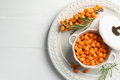 Photo of Fresh sea buckthorn berries in dish and leaves on wooden table, top view. Space for text