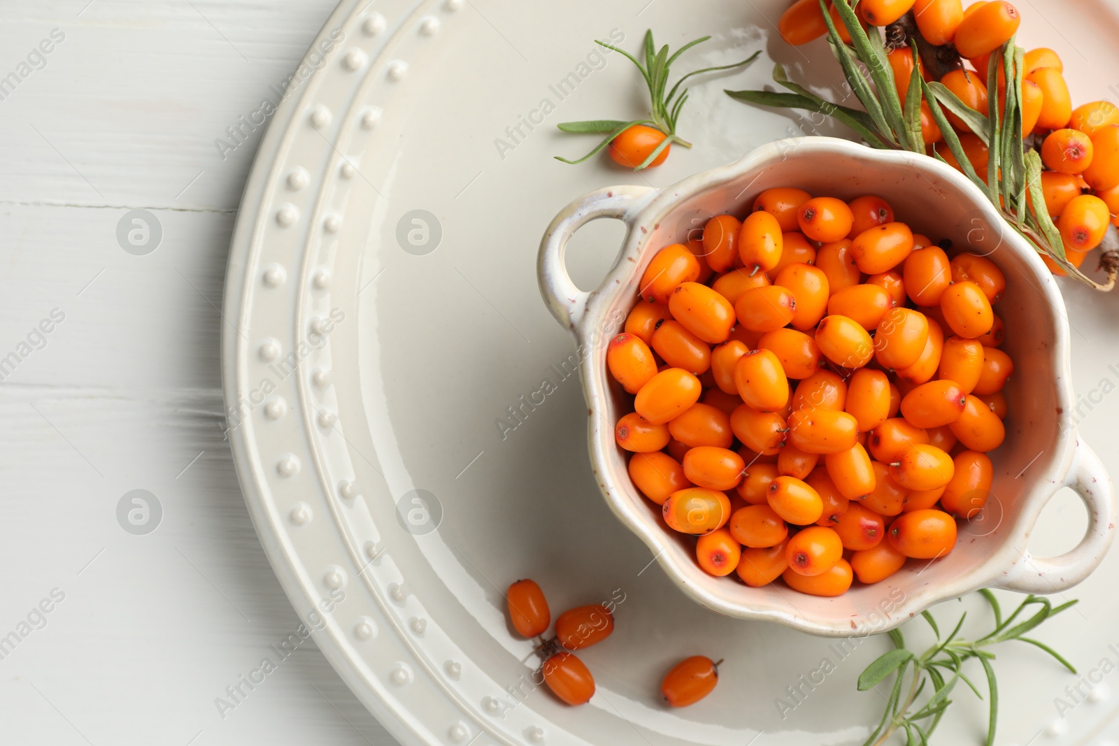 Photo of Fresh sea buckthorn berries in dish and leaves on wooden table, top view