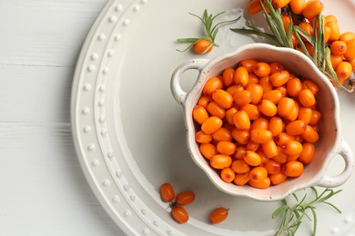 Photo of Fresh sea buckthorn berries in dish and leaves on wooden table, top view