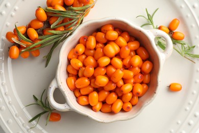 Photo of Fresh sea buckthorn berries in dish and leaves on table, flat lay