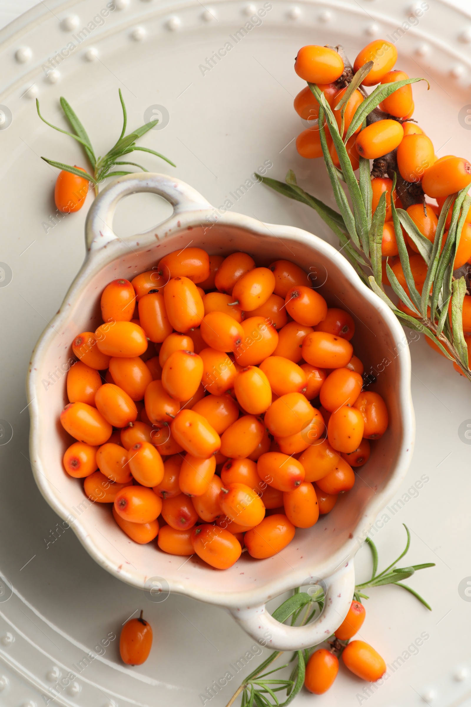 Photo of Fresh sea buckthorn berries in dish and leaves on table, flat lay