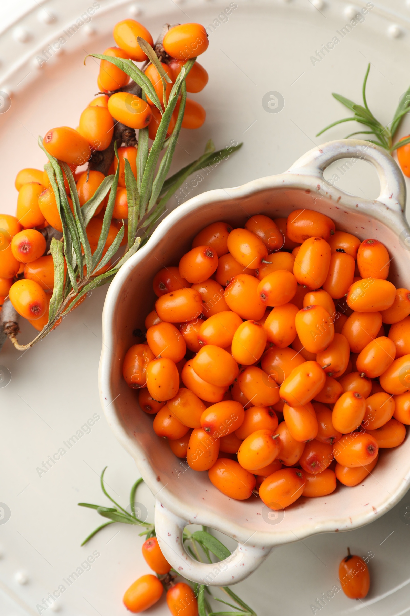 Photo of Fresh sea buckthorn berries in dish and leaves on table, flat lay