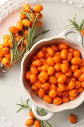 Photo of Fresh sea buckthorn berries in dish and leaves on table, flat lay