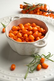 Photo of Fresh sea buckthorn berries in dish and leaves on table, closeup