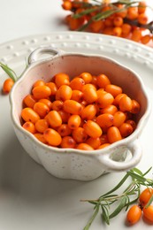 Photo of Fresh sea buckthorn berries in dish and leaves on table, closeup