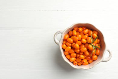 Photo of Fresh sea buckthorn berries in dish and leaves on white wooden table, top view. Space for text