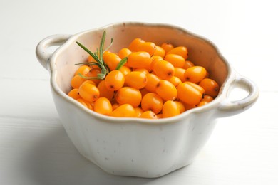 Photo of Fresh sea buckthorn berries in dish and leaves on white wooden table, closeup